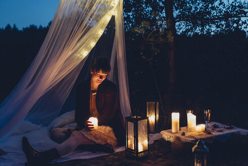 Glückliche Frau in einem romantischen Lager in herbstlicher Natur bei Kerzenlicht - MJF001739