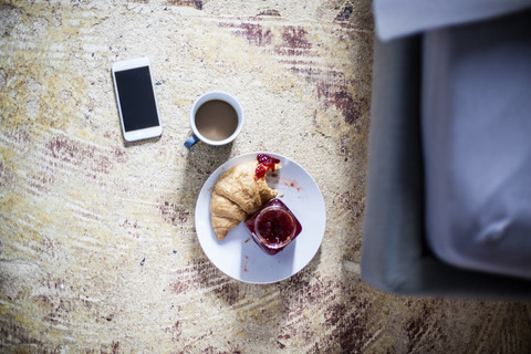 Smartphone, Tasse Kaffee und Croissant mit Marmelade auf dem Boden, lizenzfreies Stockfoto