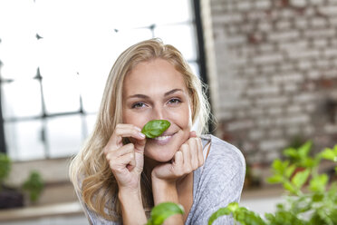 Portait of smiling blond woman holding basil leaf - FMKF002292