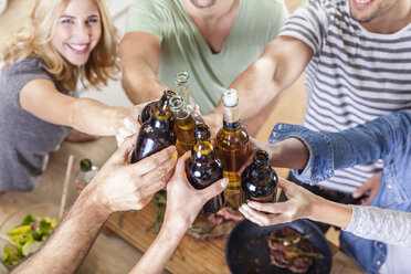 Friends clinking beer bottles in kitchen - FMKF002296