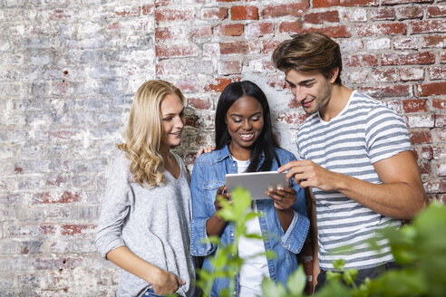 Drei lächelnde Freunde, die gemeinsam ein digitales Tablet betrachten - FMKF002320