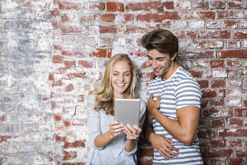 Glückliches junges Paar, das gemeinsam ein digitales Tablet betrachtet - FMKF002321