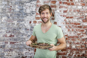 Portrait of smiling man holding board with steak - FMKF002330