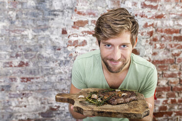 Portrait of smiling man holding board with steak - FMKF002331