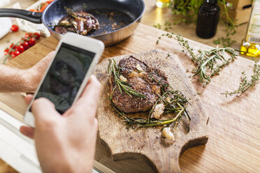 Man taking celll phone picture of prepared steaks - FMKF002335