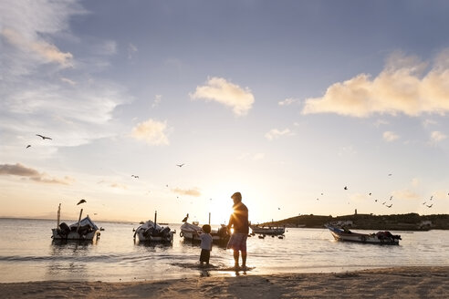 Venezuela, Isla Margarita, Juan Griego, kleiner Junge und sein Großvater stehen bei Sonnenuntergang am Meer - VABF000168