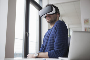 Smiling man wearing Virtual Reality Glasses in the office - RBF004086