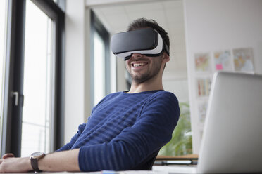 Smiling man wearing Virtual Reality Glasses in the office - RBF004087