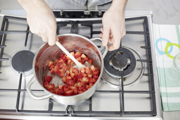 Man stirring strawberries on gas stove - FMKF002353