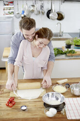 Affectionate couple preparing pizza dough in kitchen - FMKF002360