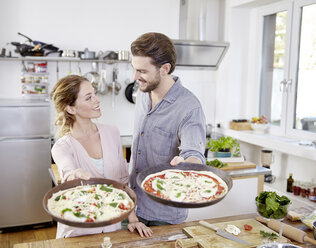 Ehepaar hält Backformen mit rohen Pizzen in der Küche - FMKF002362