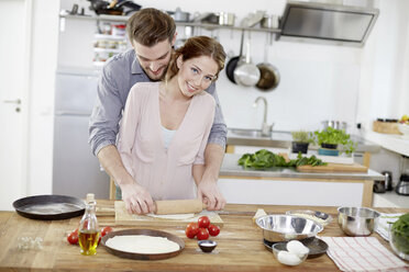 Affectionate couple preparing pizza dough in kitchen - FMKF002369