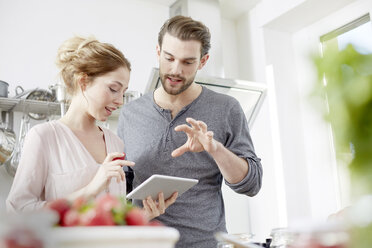 Ehepaar schaut in der Küche auf ein digitales Tablet - FMKF002378
