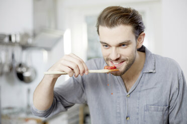 Young man tasting cooked strawberries in kitchen - FMKF002380