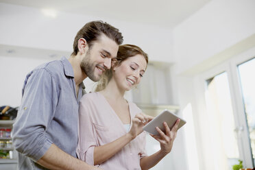 Smiling couple looking at digital tablet in kitchen - FMKF002397