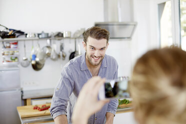 Woman taking cell phone picture of smiling man in kitchen - FMKF002402