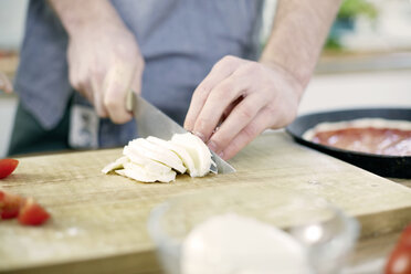 Mann schneidet Mozzarella auf einem Schneidebrett - FMKF002409