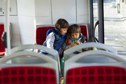 Two little boys sitting in a bus playing with smartphone stock photo