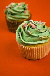 Zwei Cupcakes mit grüner Creme und Backdekor vor rotem Hintergrund - ABZF000212