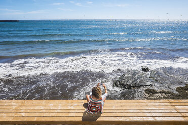 Spain, Tenerife, woman sitting on a bench in front of the sea taking a picture with her smartphone - SIPF000199