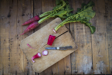 Sliced organic red radish and a pocket knife on wooden board - LVF004568