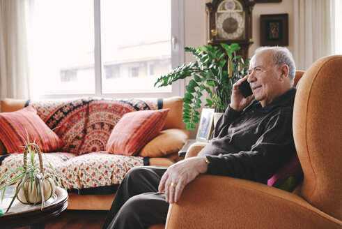 Portrait of smiling senior man telephoning with smartphone at home - GEMF000748