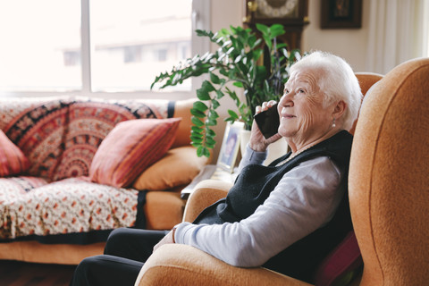 Lächelnde ältere Frau, die zu Hause mit ihrem Smartphone telefoniert, lizenzfreies Stockfoto