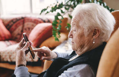 Ältere Frau sitzt im Wohnzimmer und benutzt ihr Smartphone - GEMF000753