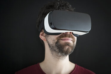 Smiling man wearing Virtual Reality Glasses in front of black background - RBF004095