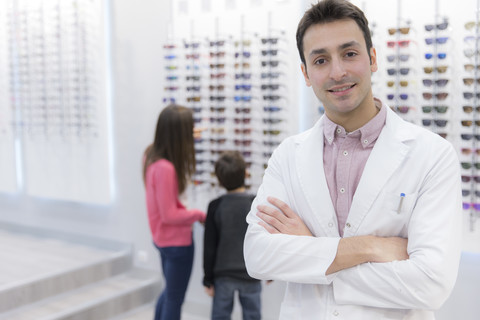 Portrait of smiling optician in shop with people in background stock photo