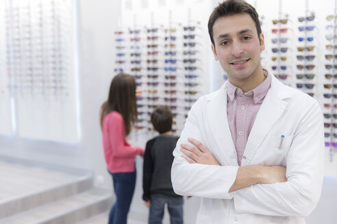 Porträt eines lächelnden Optikers in einem Geschäft mit Menschen im Hintergrund - ERLF000141