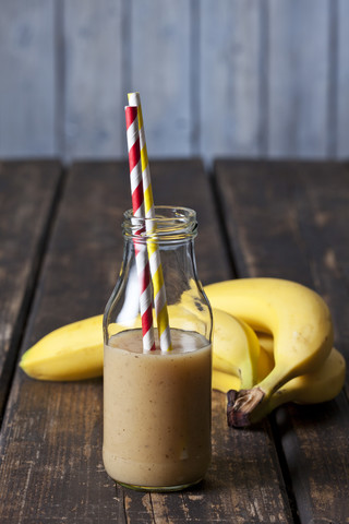 Glasflasche mit Bananensmoothie und drei Bananen auf Holz, lizenzfreies Stockfoto