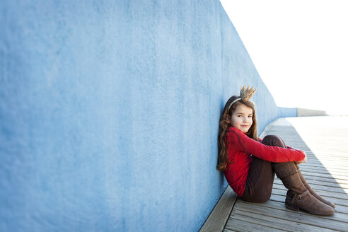 Portrait of little girl with a crown leaning against blue wall - VABF000207