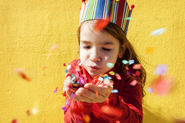 Portrait of little girl wearing paper crown blowing confetti - VABF000211