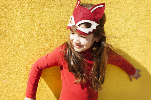 Porträt eines kleinen Mädchens mit Tiermaske vor einer gelben Wand, lizenzfreies Stockfoto