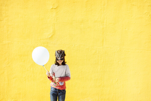 Portrait of little girl with balloon wearing animal mask in front of yellow wall - VABF000215