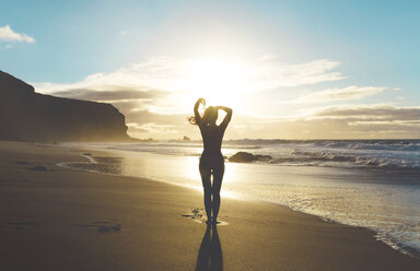 Woman standing on the beach with hands on head at sunset - GEMF000756