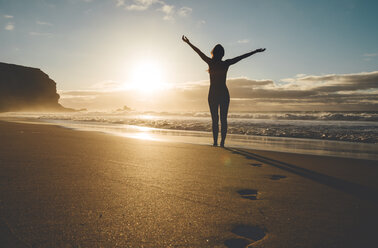 Woman standing on the beach with raised arms at sunset - GEMF000760