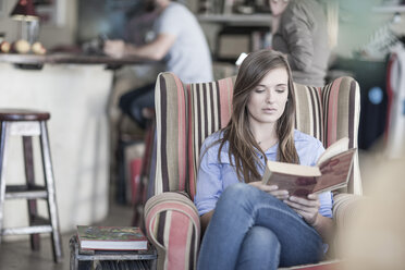 Junge Frau sitzt in einem Café und liest ein Buch - ZEF008549