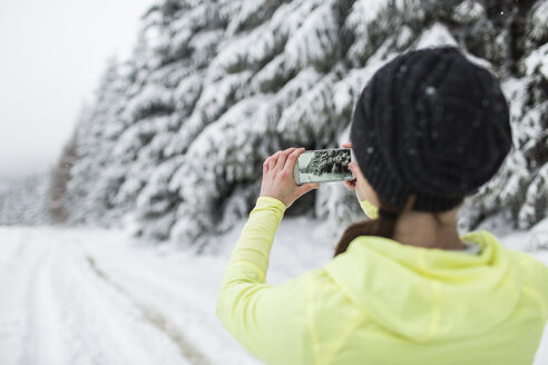 Frau auf verschneiter Straße beim Fotografieren mit dem Smartphone - HAPF000261