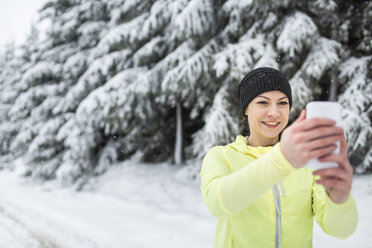 Frau auf verschneiter Straße beim Fotografieren mit dem Smartphone - HAPF000262