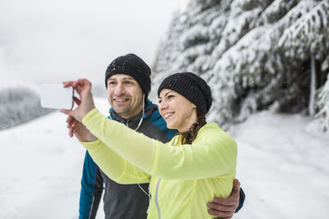Paar in Winterlandschaft nimmt Selfie mit Smartphone - HAPF000263