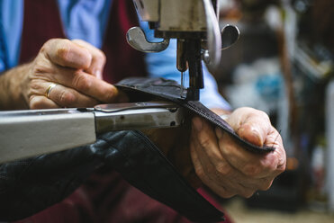 Shoemaker sewing a shoe with machine in his workshop, close-up - KIJF000195