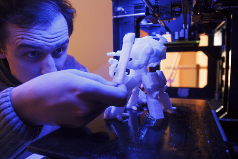 Mann, der eine mit einem 3D-Drucker gedruckte Roboterfigur untersucht - ABZF000219