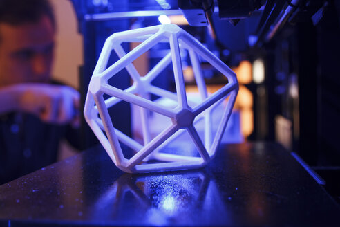 geometrische 3D-Figur auf der Plattform eines 3D-Druckers mit einem Mann im Hintergrund - ABZF000221