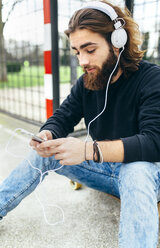 Porträt eines bärtigen jungen Mannes mit Smartphone und Kopfhörern - MGOF001460
