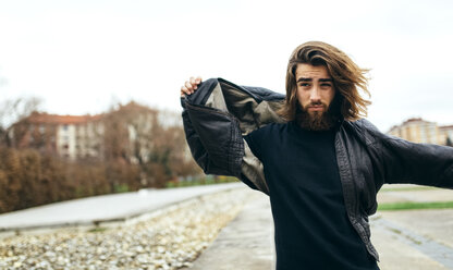 Portrait of bearded young man putting on his leather jacket - MGOF001463