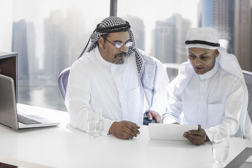 Zwei Geschäftsleute aus dem Nahen Osten sitzen im Büro und schauen auf ein digitales Tablet - ZEF008562
