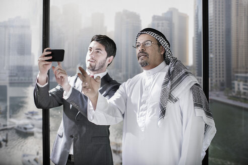 Geschäftsleute aus dem Westen und dem Nahen Osten diskutieren über die Zukunft und halten ein Smartphone in der Hand - ZEF008574
