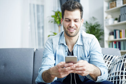 Young man at home with smartphone and earbuds - SEGF000435
